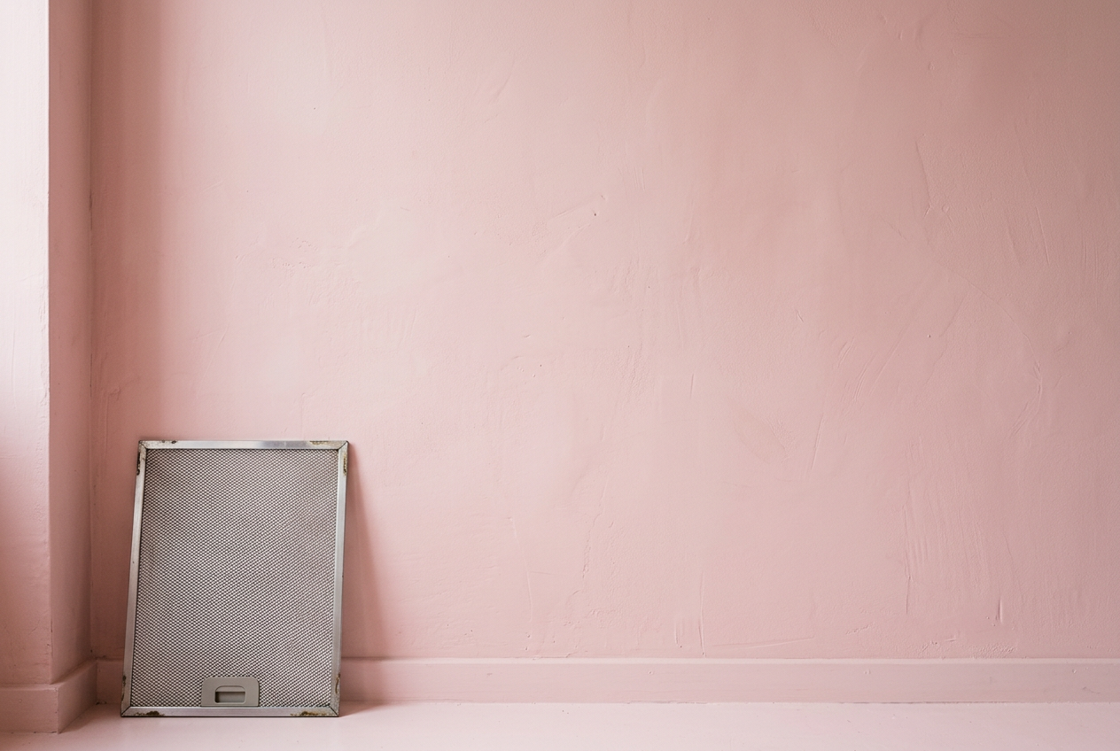 Un mur rose avec un filtre de hotte en inox posé contre lui
